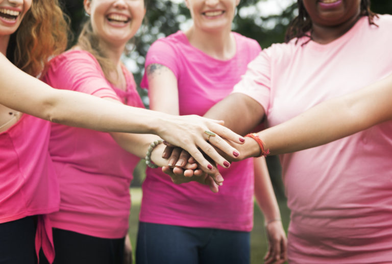 Mamografia digital. Imagem mostra mulheres unindo as mãos com camisas rosas