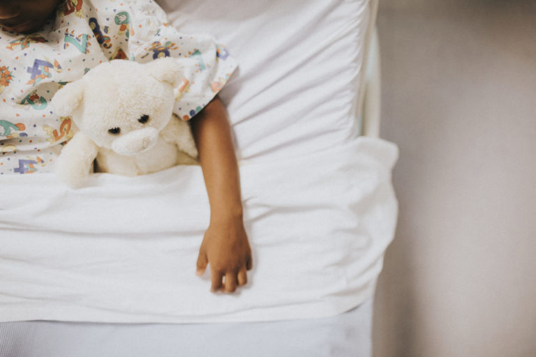 Criança na cama segurando um urso de pelúcia no braço