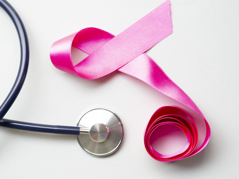 estetoscópio ao lado de fita rosa formando um laço em representação ao câncer de mama