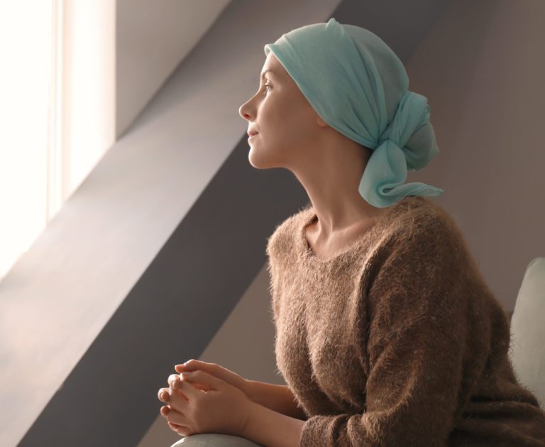 mulher com câncer dentro de casa olhando pela janela